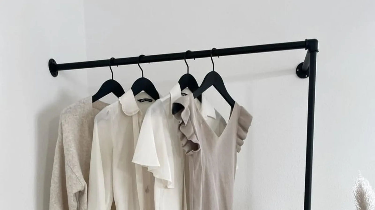 Schwarze Kleiderstange stabil an einer Wand montiert, mit Kleidung auf Bügeln